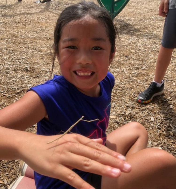 Young girl holding an insect on her hand outside at Kid's Resort